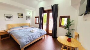 A bedroom with a wooden bed, a small table with a red mug, a potted plant, and a window with curtains. - Entire Home: Beautiful, Brand-new built in 2022 (Phuong 6, Da Lat city)