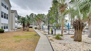 A pathway leading to a building with a modern design, surrounded by palm trees and a gravel area. - 2 Mi to Surfside Beach! Condo w/ Community Pool (Myrtle Beach)