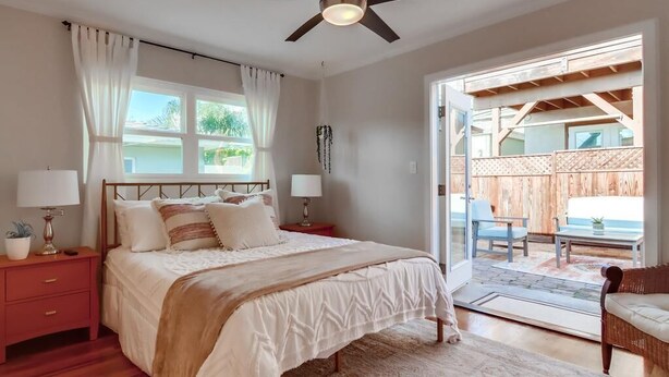 A bedroom with a bed, bedside tables, a ceiling fan, and a view to an outdoor patio area. - Ocean view! Walk to Sunset Cliffs - Surf - Beach! (San Diego)