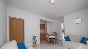 A living room with a sofa, a dining table with chairs, and a kitchen in the background. - Apartments Anamarija - One Bedroom Apartment with Balcony (Privlaka)