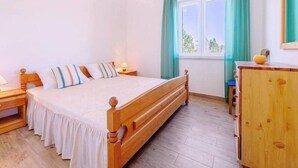 A bedroom with a wooden bed, a nightstand, a dresser, and a window with curtains. - Apartments Anamarija - One Bedroom Apartment with Balcony - 2 (Privlaka)