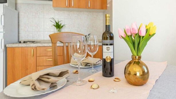 A dining table with a bottle of wine, a vase of tulips, and empty wine glasses. - Apartments Anamarija - One Bedroom Apartment with Balcony - 2 (Privlaka)