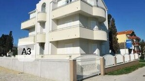A multi-story residential building with balconies, a gated entrance, and a clear blue sky in the background. - Apartments Anamarija - One Bedroom Apartment with Balcony - 2 (Privlaka)