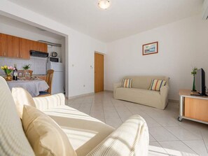 Ein Wohnzimmer mit einer Couch, einem Esstisch mit Stühlen, einer Küchenzeile und einem Fernseher auf einem Schrank.
