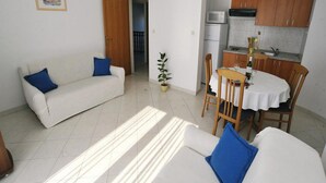 Un soggiorno con un divano bianco e cuscini blu, un tavolo da pranzo con sedie e un angolo cottura con mobili in legno ed elettrodomestici.