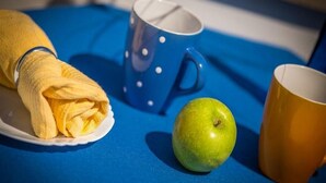 Ett blått bord med en gul handduk, ett grönt äpple och två muggar.