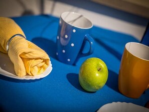 Uma mesa azul com uma toalha amarela, uma maçã verde e duas canecas.