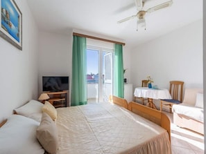 Habitación de hotel con cama, televisión, mesa de comedor con sillas y balcón con cortinas.
