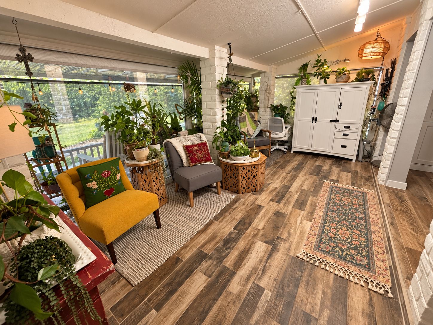 A cozy indoor space with a wooden floor, a yellow armchair, a gray sofa, and various potted plants.