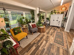 A cozy indoor space with a wooden floor, a yellow armchair, a gray sofa, and various potted plants.