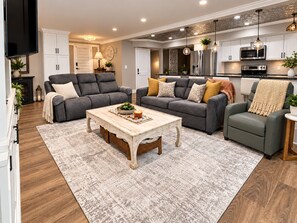 A modern living room with a fireplace, sofas, a coffee table, and a kitchen area with appliances.