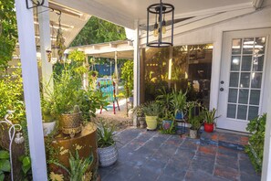 A covered outdoor area with potted plants, a wooden bench, and a door leading inside. - Tropical Garden Oasis  • Birdwatcher's Paradise • Spacious Harlingen Retreat (Harlingen)