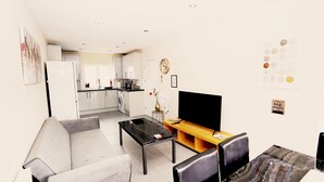 Ein kompakter Wohnraum mit Küchenzeile, einem Essbereich mit Fernseher und einer Couch.