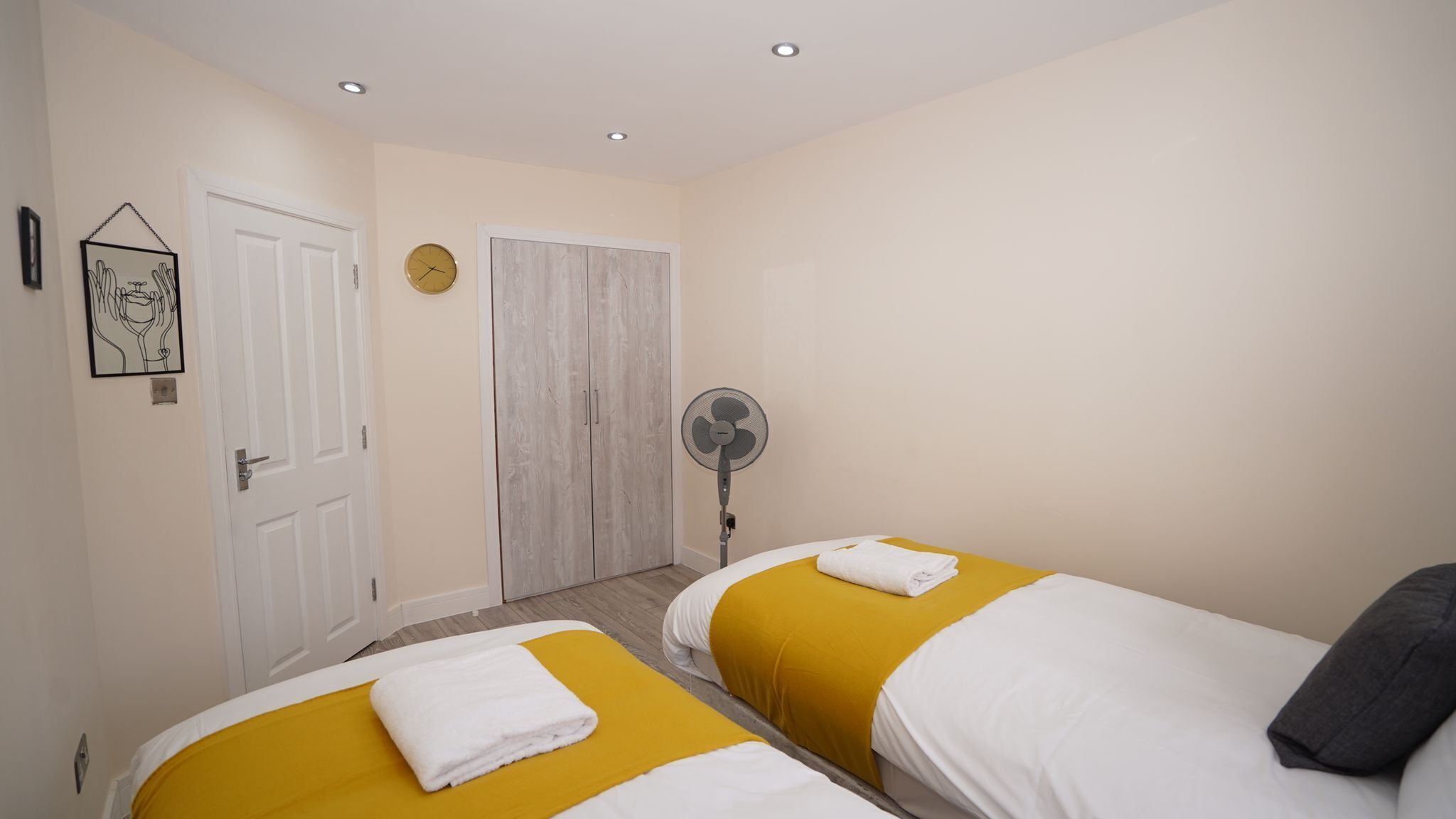 Een hotelkamer met twee bedden, een deur, een ventilator en een klok aan de muur.