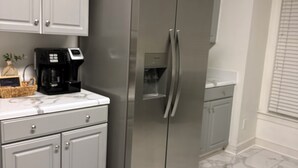 Eine Küche mit grauen Schränken, einem Edelstahl-Kühlschrank, einer Kaffeemaschine und Marmorböden.