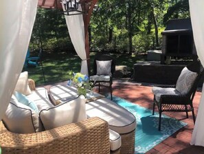 Ein überdachter Patio-Bereich mit Korbmöbeln, einem Grill und Blick ins grüne Umland.