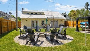 Un patio trasero con un brasero, sillas Adirondack y un área de patio techada.