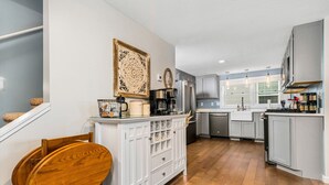 Una cocina moderna con armarios blancos, una mesa de comedor de madera y una cafetera.