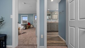 Un pasillo que conduce a un dormitorio con vistas, una cocina con gabinetes grises y un baño con espejo.