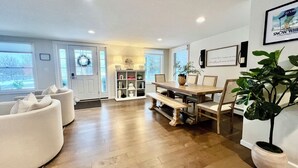 Un salón amplio con una mesa y sillas de madera, un sofá blanco y una planta grande en maceta.
