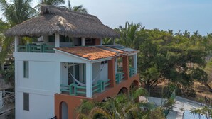 A two-story building with a thatched roof, a balcony, and a view of the surrounding greenery. - Staffed Ocean-View Villa · Private Pool · Starlink · 2 Min to Zicatela (Puerto Escondido)
