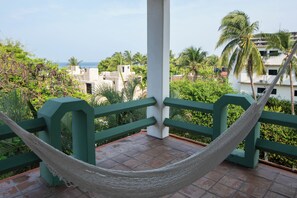 Un hamac sur un balcon avec vue sur des palmiers et des immeubles.