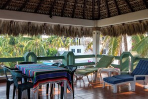 Un espace extérieur abrité, aménagé avec une table, des chaises et offrant une vue sur les palmiers et les bâtiments.