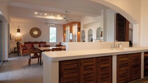 A modern kitchen with a large island, wooden cabinets, and a dining area with a sofa and chairs. - Staffed Ocean-View Villa · Private Pool · Starlink · 2 Min to Zicatela (Puerto Escondido)