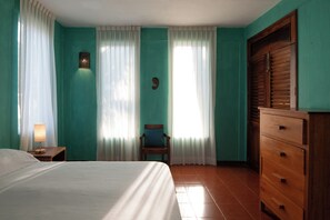 Ein Schlafzimmer mit Bett, Stuhl, Kommode und Vorhängen.