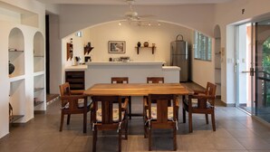 A dining area with a wooden table and chairs, a kitchen in the background, and a view through a glass door. - Staffed Ocean-View Villa · Private Pool · Starlink · 2 Min to Zicatela (Puerto Escondido)