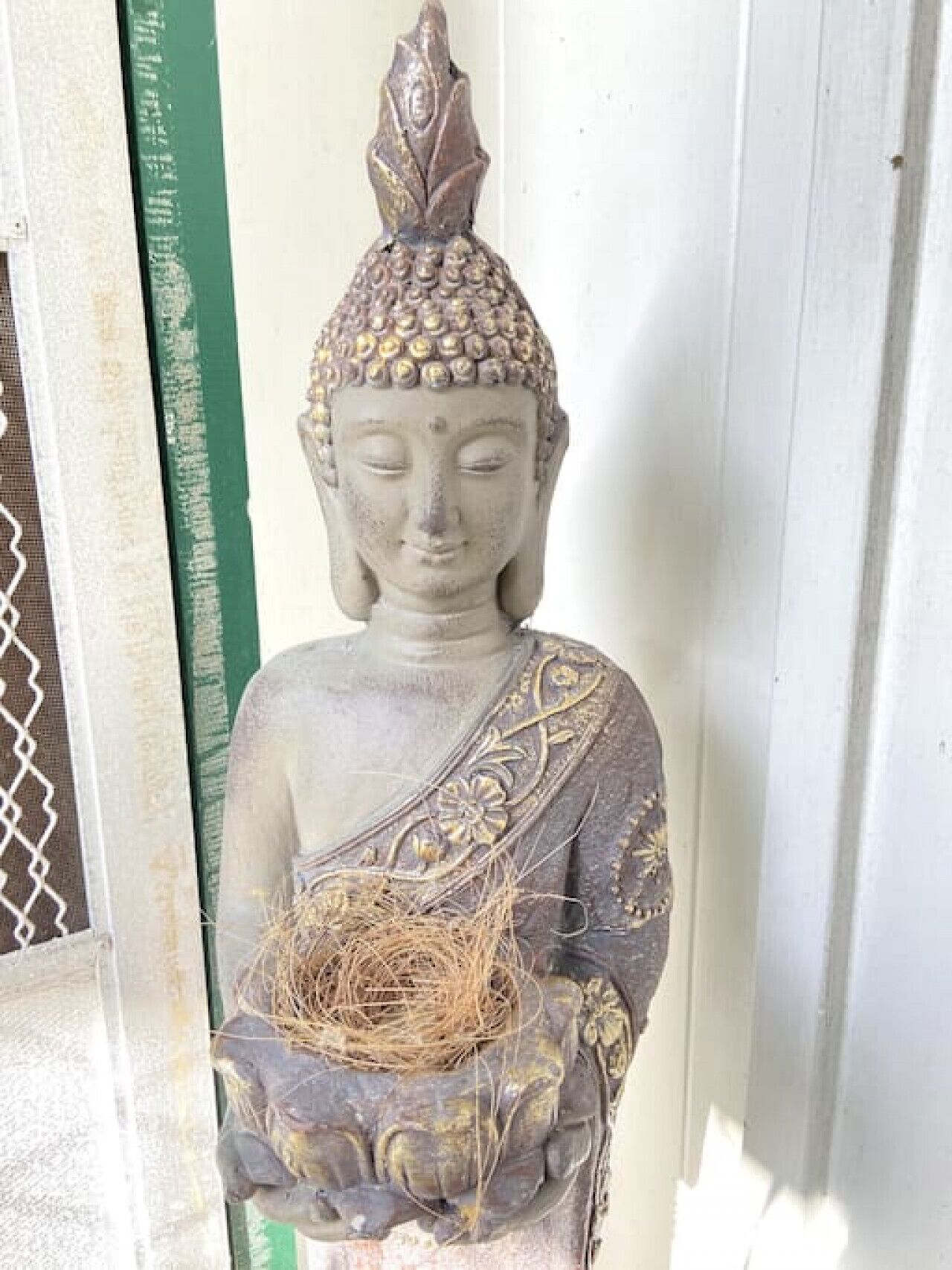 A statue of a seated figure with a lotus flower in its lap, placed against a white wall.