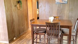 A dining area with a wooden table and chairs, a hanging light fixture, and a painting on the wall.