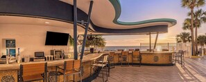 Un bar frente al mar con techo curvo, asientos exteriores y vistas al océano.