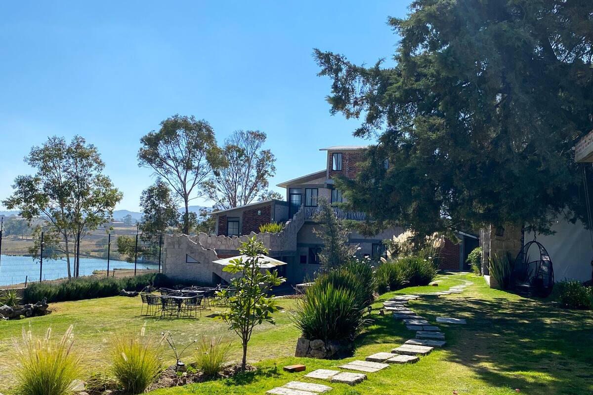 Una casa moderna con un camino de piedra, un patio con mobiliario exterior y vistas a una masa de agua.
