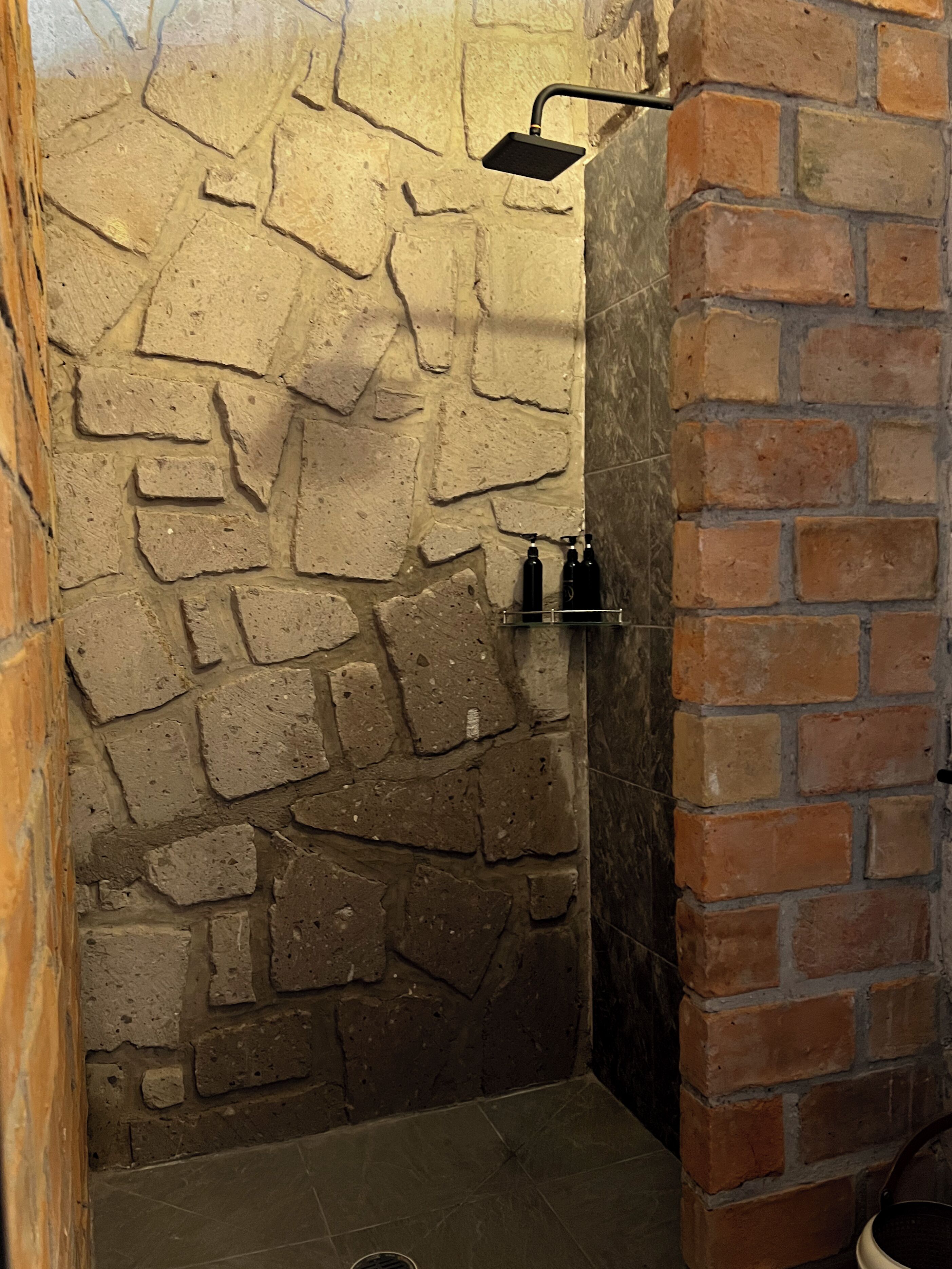 Baño con pared de piedra, zona de ducha e instalación de suelo de baldosas.