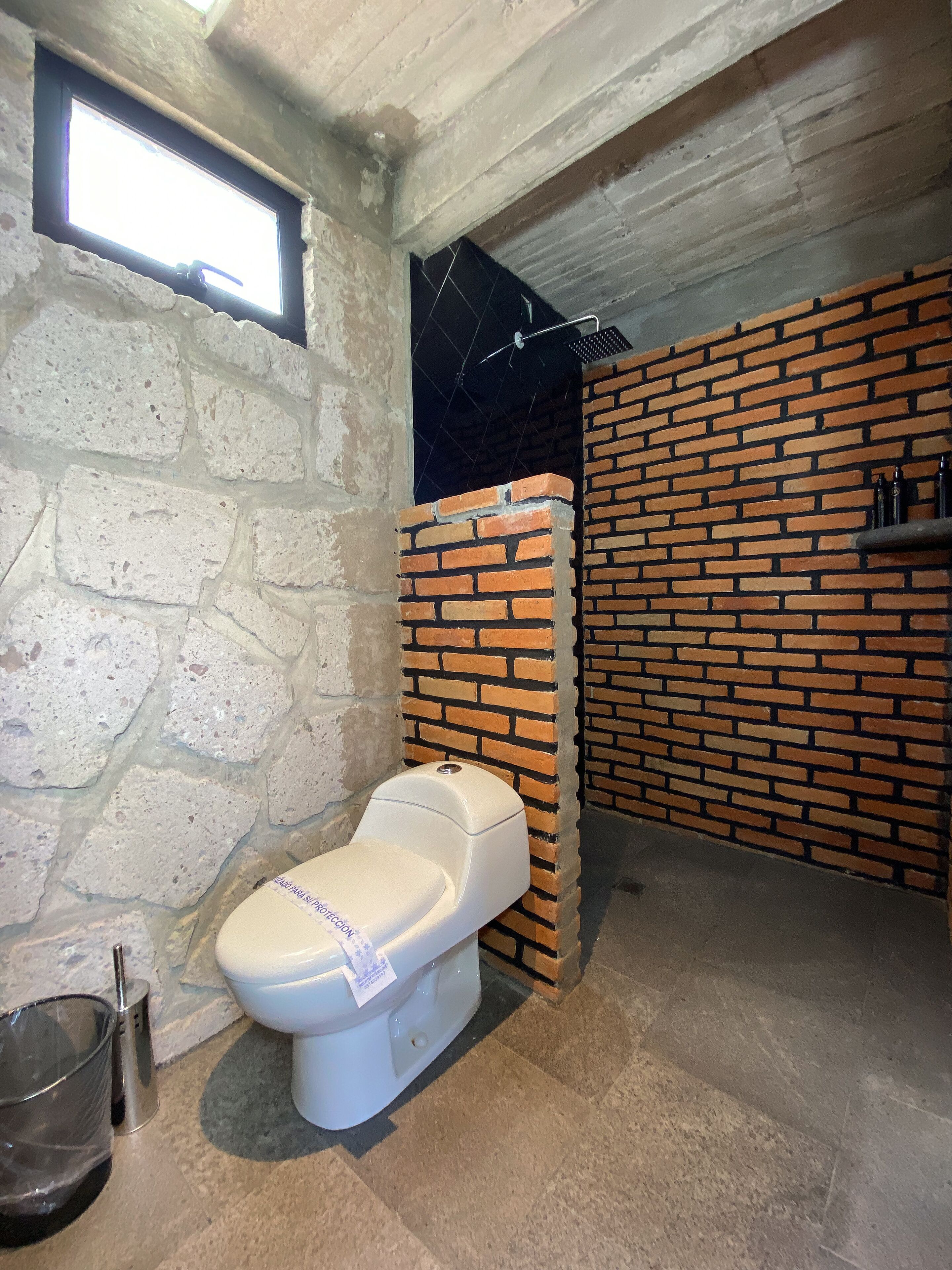 Un baño con inodoro, ventana y pared de ladrillo.