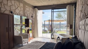 Un dormitorio con pared de piedra, una cama grande, un sofá, una bañera y vistas a un lago.