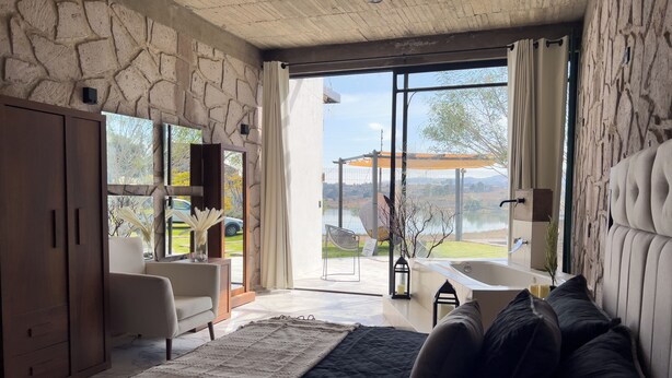 Un dormitorio con pared de piedra, una cama grande, un sofá, una bañera y vistas a un lago.