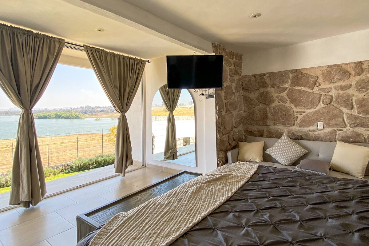 Un dormitorio con una cama grande, pared de piedra y vistas a un cuerpo de agua.