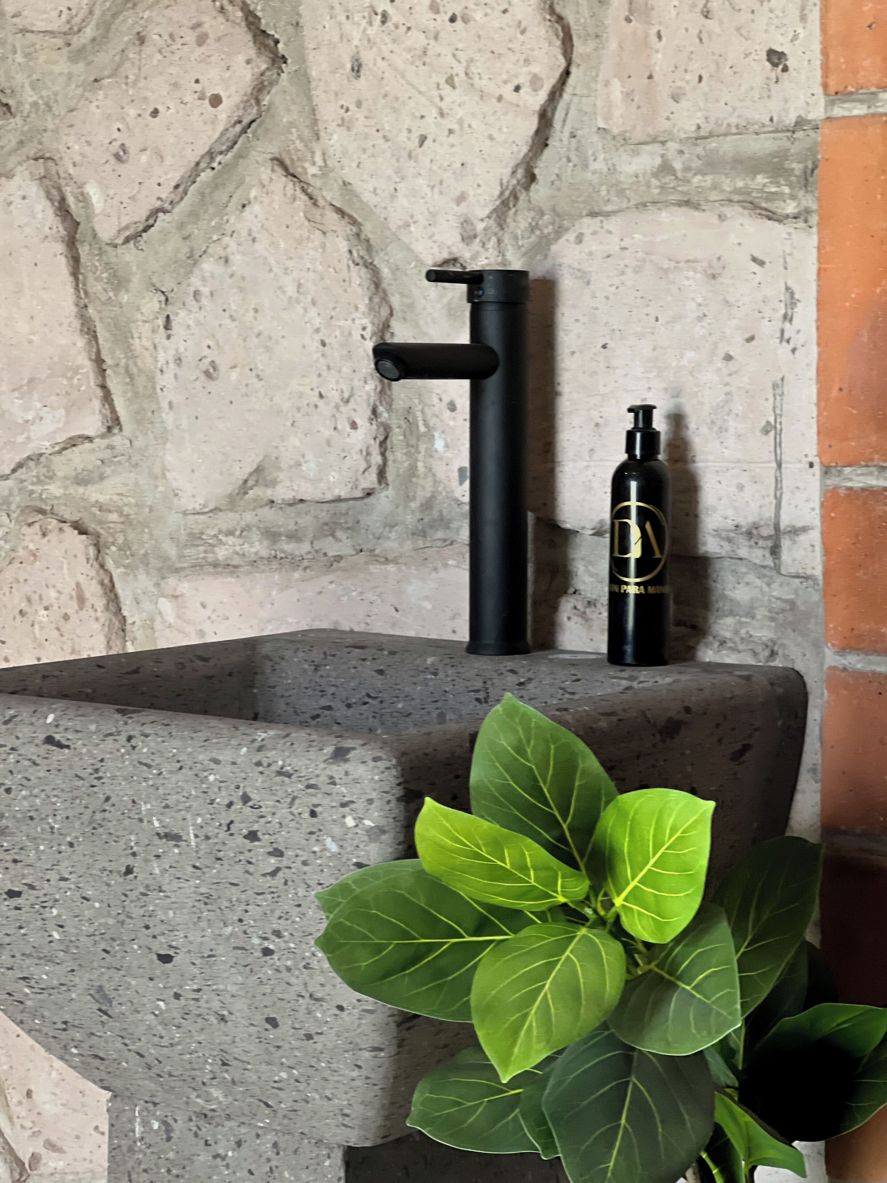 A stone sink with a black faucet and a black bottle with a gold logo.