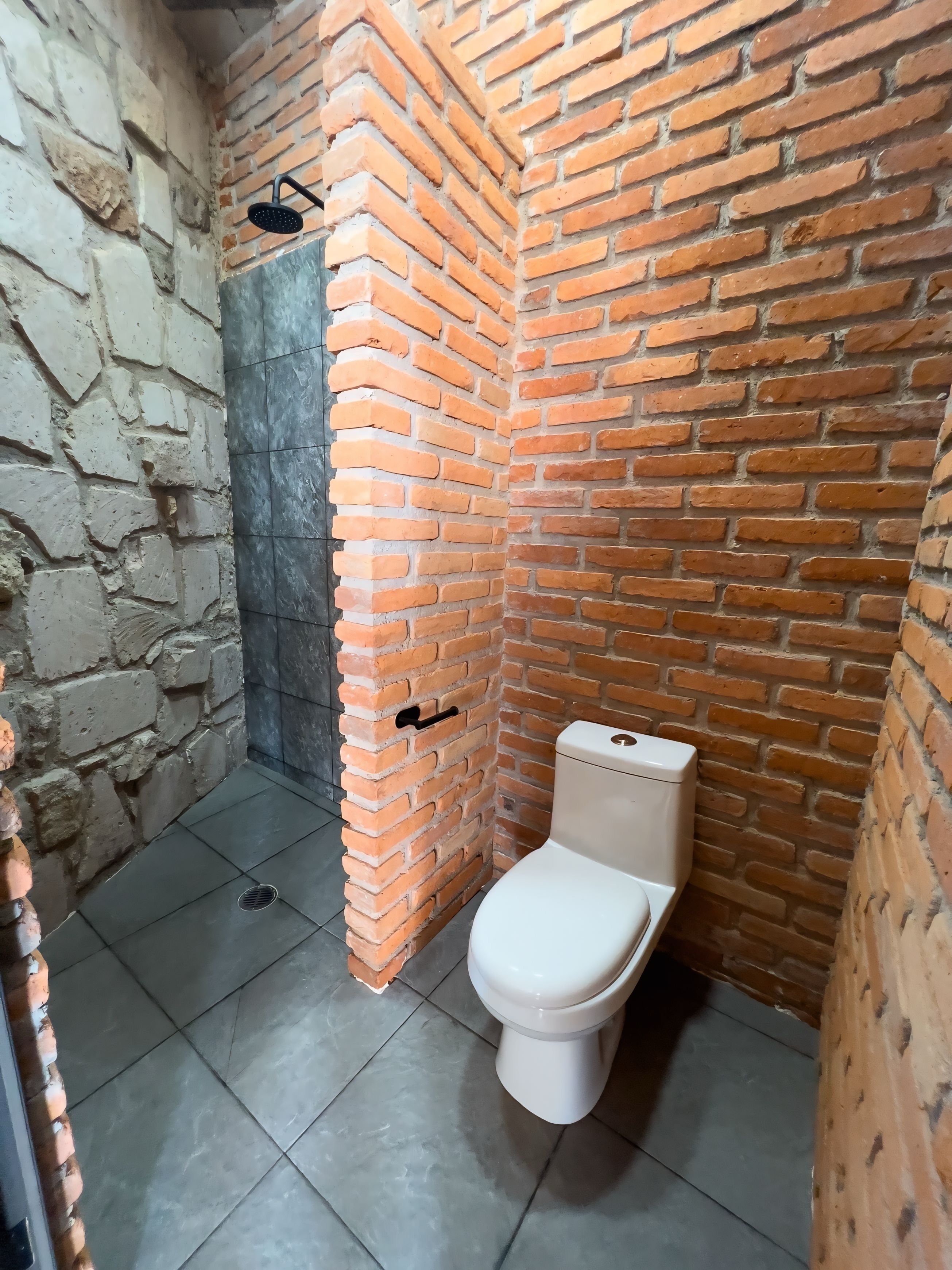 A bathroom with a toilet, a shower, and a stone wall.