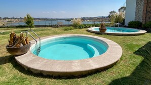 Un área de piscina con dos piscinas circulares, un hogar para fuego y vistas a un lago y colinas distantes.