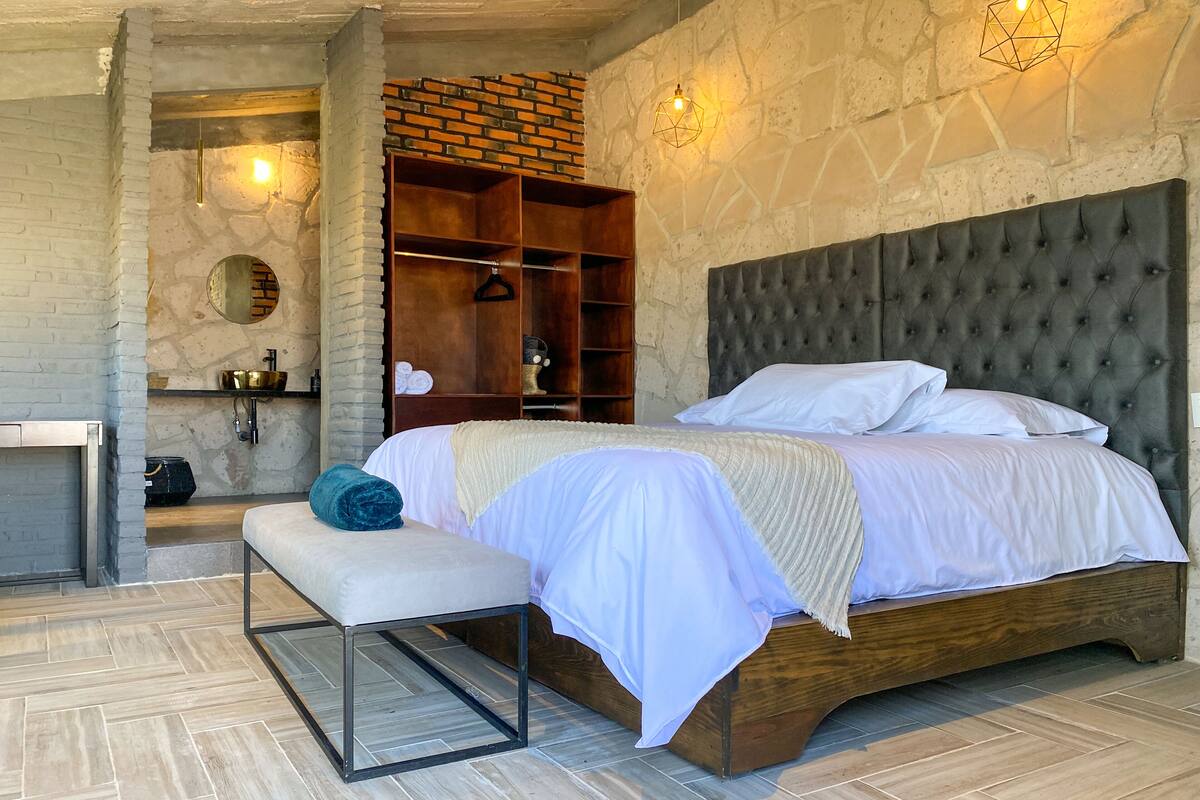 Un dormitorio moderno con una cama grande, un banco, un armario de madera y una pared de piedra.