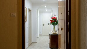Entrada de hotel con un felpudo que dice “BIENVENIDOS”, un mostrador de recepción de madera y un pasillo que conduce a las habitaciones.