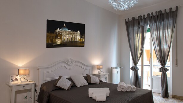 Un dormitorio ordenado con una cama grande, dos mesitas de noche con lámparas, un cuadro en la pared y vistas por la ventana.