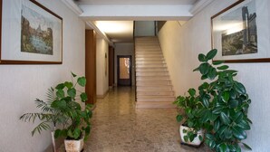Un pasillo con cuadros enmarcados en las paredes, una escalera y plantas en macetas.