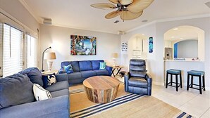 A modern living room with a sectional sofa, a round coffee table, a recliner, and a dining area with bar stools.
