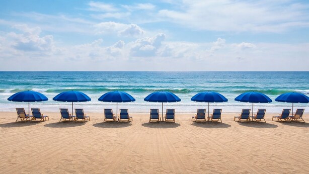 A beach with rows of blue umbrellas and lounge chairs facing the ocean.