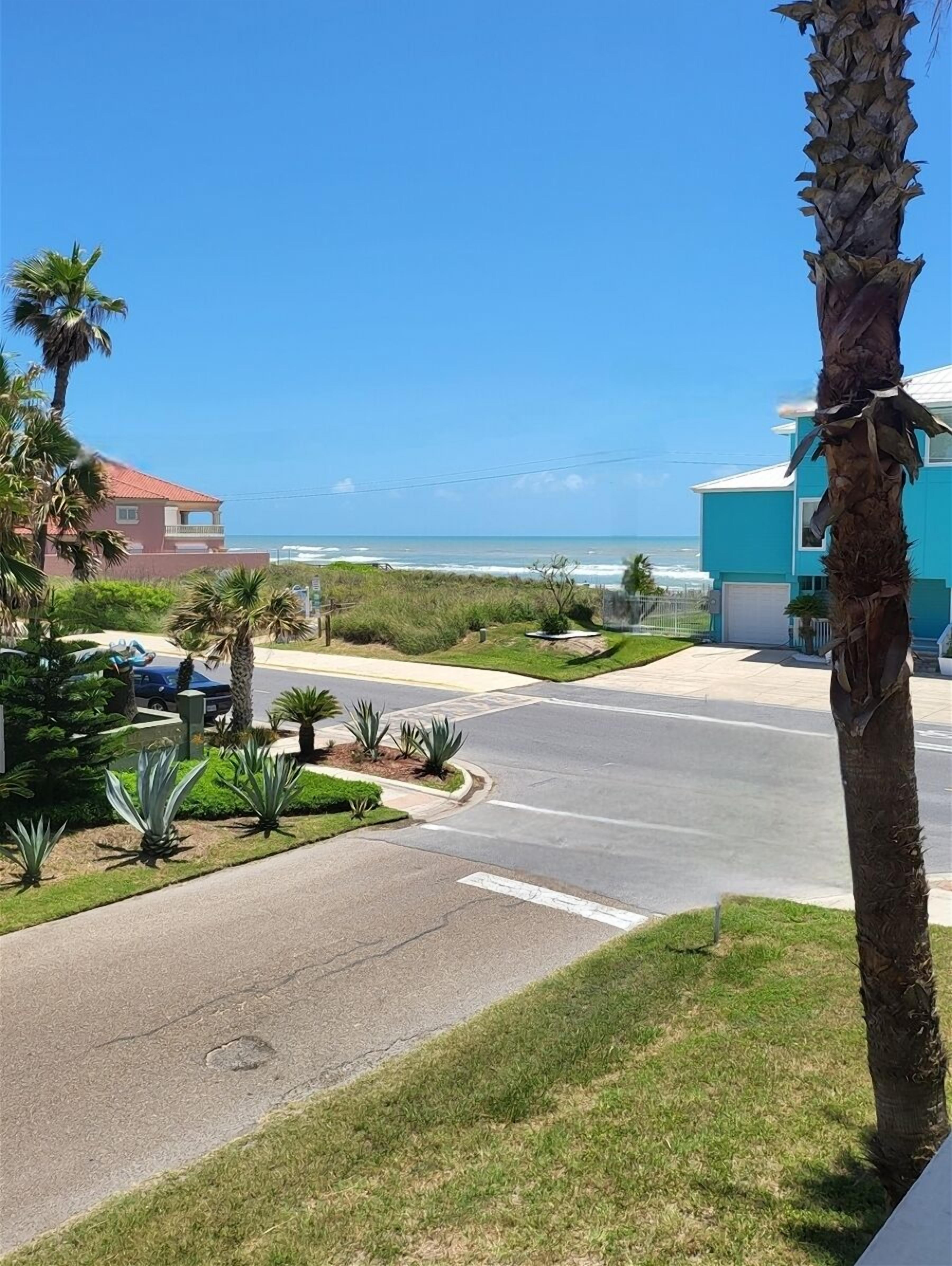Een woonstraat met uitzicht op de oceaan, palmbomen en huizen.