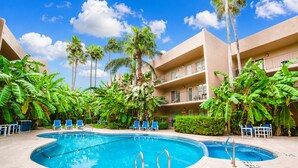 A pool area with two pools, palm trees, and a building with balconies. - Beach View Condo 106 By The Beach  Heated Pool Hot tub (South Padre Island)